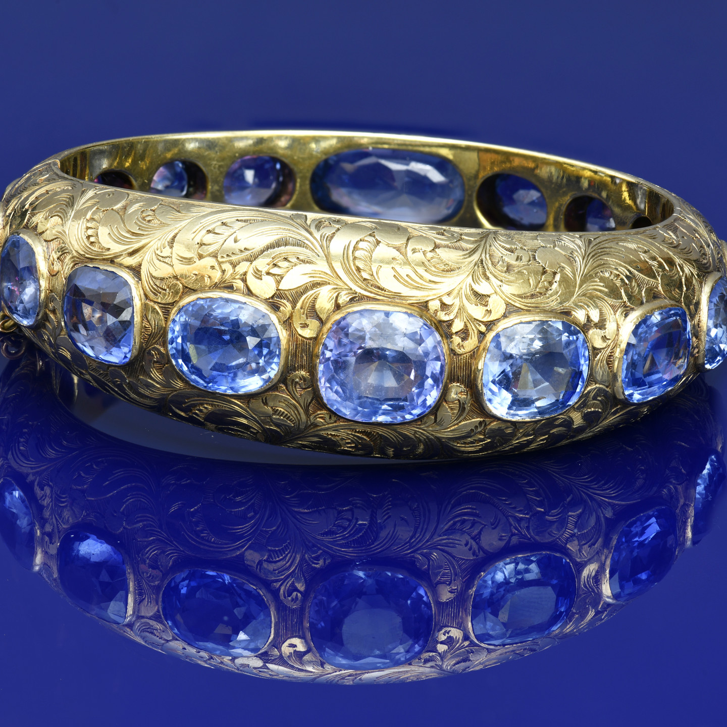 A c1900 18ct gold bangle with engraved floral decoration, set with seventeen cushion cut Ceylon Sapphires, the total sapphire weight approximately 68ct, 55.3g