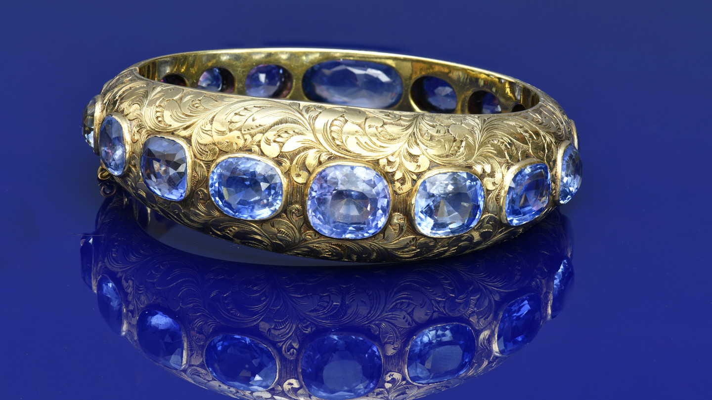 A c1900 18ct gold bangle with engraved floral decoration, set with seventeen cushion cut Ceylon Sapphires, the total sapphire weight approximately 68ct, 55.3g