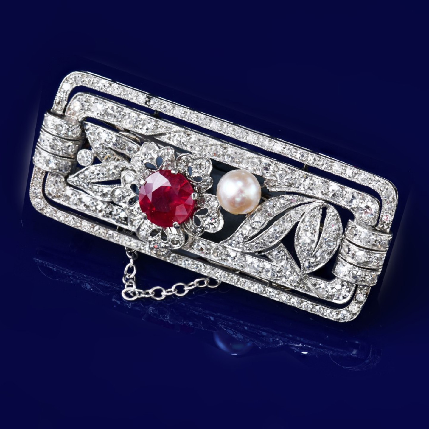 An Art Deco platinum brooch set with a round cut ruby of approximately 1.2ct, a natural pearl (5mm) and round cut diamonds, 12g, 4.3 x 1.9cm