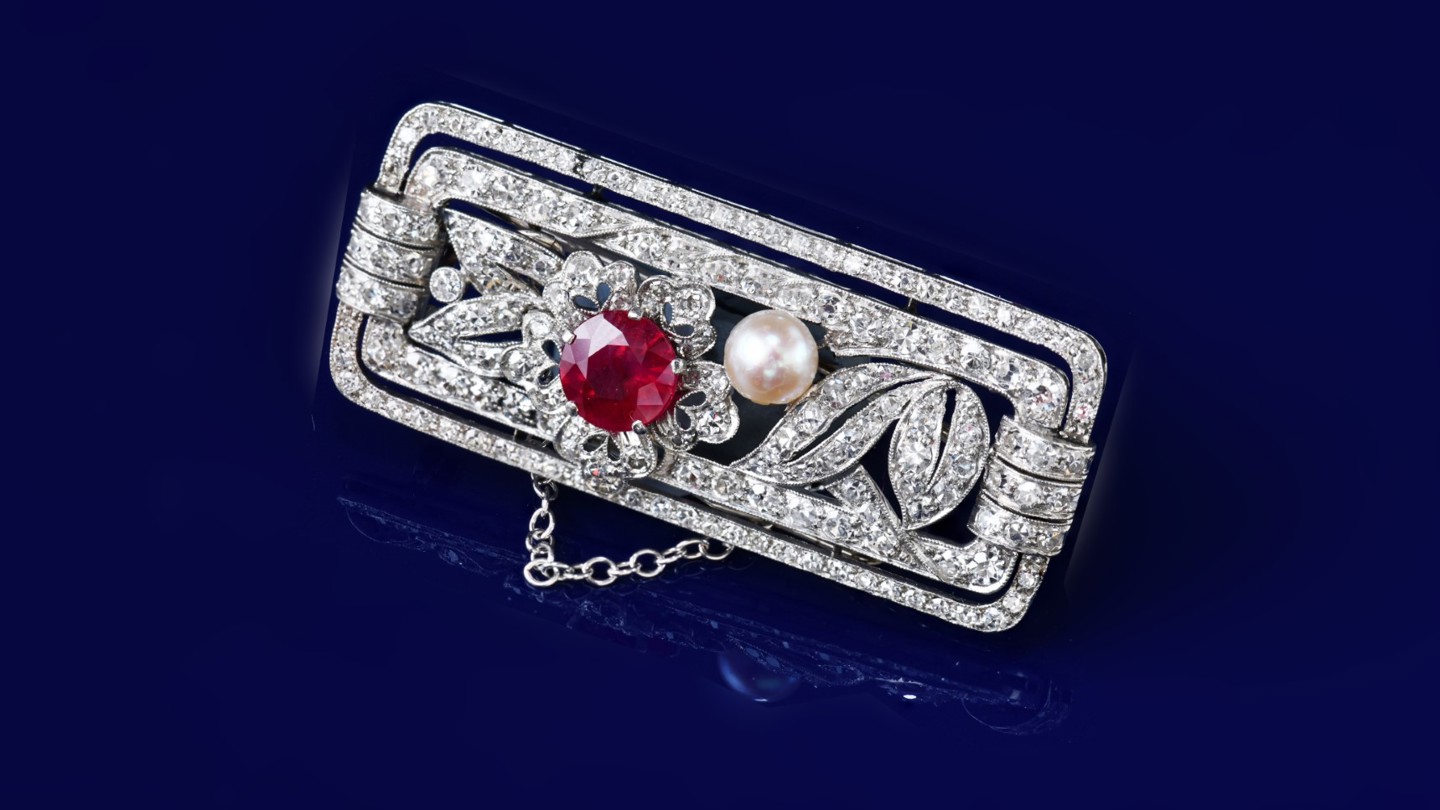An Art Deco platinum brooch set with a round cut ruby of approximately 1.2ct, a natural pearl (5mm) and round cut diamonds, 12g, 4.3 x 1.9cm