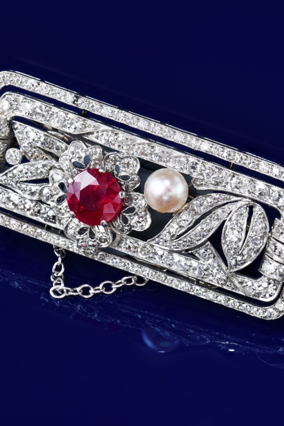 An Art Deco platinum brooch set with a round cut ruby of approximately 1.2ct, a natural pearl (5mm) and round cut diamonds, 12g, 4.3 x 1.9cm